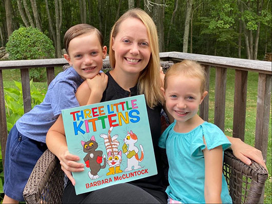 smiling librarian with her two children holding Three Little Kittens book
